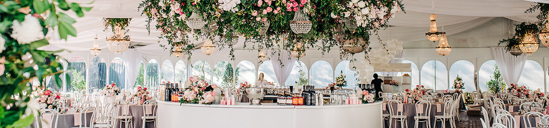 White rounded bar inside a marquee set up for a wedding, with a floral installation hanging from the ceiling.